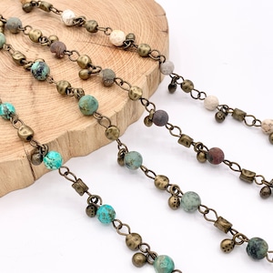 May include: Four strands of beaded chain with different colored beads. The beads are a mix of brown, white, and turquoise. The chain is made of brass.