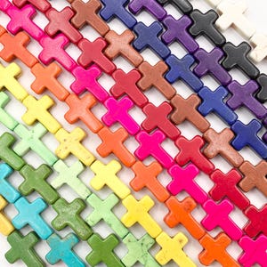 May include: Rows of colorful cross-shaped beads in various shades, including pink, orange, yellow, green, blue, purple, brown, black, and white. The beads are arranged diagonally, showcasing a spectrum of colors and textures, ideal for jewelry making.
