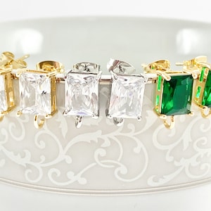 May include: Four pairs of earrings with square-shaped stones. Two pairs have clear stones, one pair has green stones, and one pair has a gold setting.