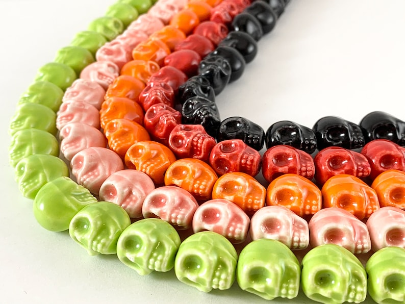 May include: A colorful strand of ceramic skull beads in shades of green, pink, orange, red, and black. The beads are arranged in a rainbow pattern.