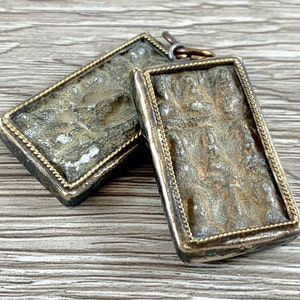 May include: Two rectangular silver pendants with a gold trim. The pendants have a textured surface and appear to be antique.