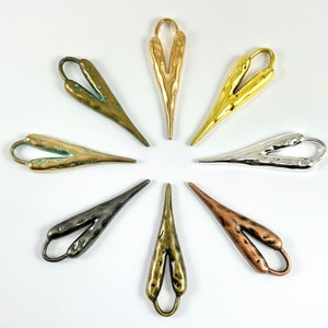 May include: Eight heart-shaped metal charms in different finishes, including silver, gold, bronze, and copper. The charms are arranged in a circle on a white background.