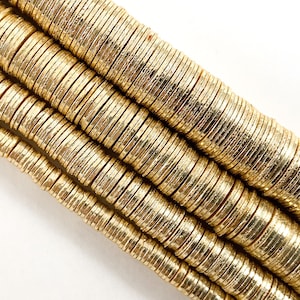 May include: A close-up of a strand of gold-colored metal beads. The beads are round and flat, and they are stacked on top of each other.
