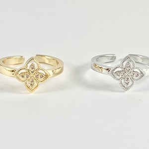 May include: Two adjustable rings with a four-leaf clover design. The ring on the left is gold with clear stones, and the ring on the right is silver with clear stones.