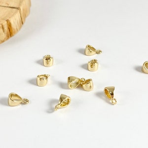 May include: A collection of eight gold-toned metal pendant bails, some with a loop shape and others with a teardrop shape.