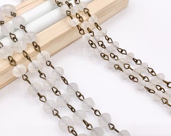 May include: Three strands of white glass beads strung on a brass chain. The beads are faceted and have a frosted appearance.