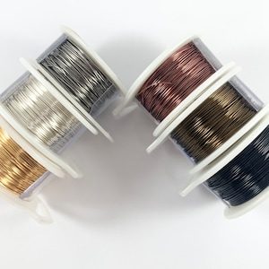May include: Five spools of wire in different colors: silver, gold, copper, black, and brass. The spools are stacked on top of each other.
