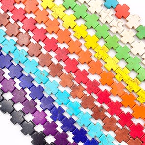 May include: A rainbow assortment of cross-shaped gemstone beads. The beads are made of turquoise, lapis lazuli, purple, black, red, orange, yellow, green, and white.