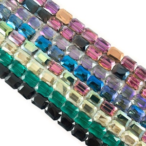 May include: Rows of faceted rectangular beads in a variety of colors, including black, green, blue, purple, and gold, are arranged diagonally against a white background. The beads have a reflective, iridescent quality.