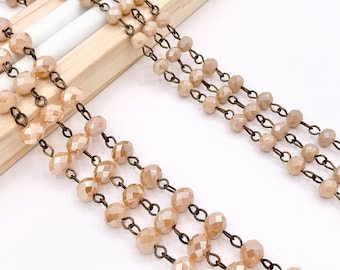 May include: A strand of light brown faceted glass beads strung on a bronze chain. The beads are evenly spaced and the chain is visible between each bead.