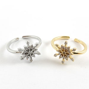May include: Two adjustable rings with a snowflake design. The ring on the left is silver and the ring on the right is gold.