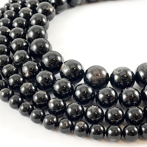 May include: A strand of black gemstone beads, with a high-gloss finish. The beads are round and uniform in size, and they are strung on a clear thread. The beads are arranged in a circular pattern, and they are all of the same size.