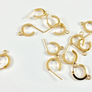 May include: A group of 10 gold-toned earring hoops with a post and a small loop on the other end. The hoops are scattered on a white surface.