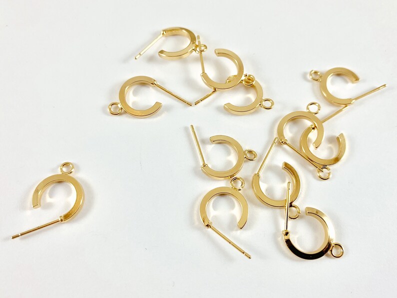 May include: A group of 10 gold-toned earring hoops with a post and a small loop on the other end. The hoops are scattered on a white surface.