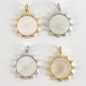 May include: Four gold and silver pendants with a white mother of pearl center and a circle of clear rhinestones around the edge. The pendants are in the shape of a sun with points around the edge.