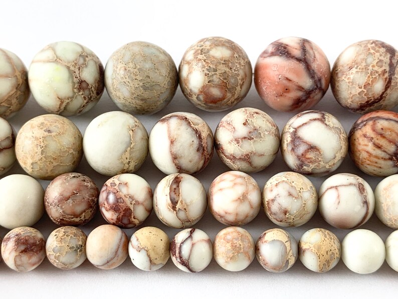 May include: A strand of round, brown, white, and pink jasper beads. The beads have a mottled, marbled appearance.