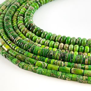 May include: A collection of green jasper beads in various shapes and sizes. The beads are arranged in a circular pattern, with the largest beads at the bottom and the smallest beads at the top.
