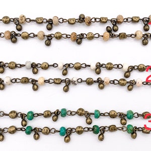May include: Three strands of chain necklaces with different colored beads. The top strand has brown and white beads, the middle strand has white beads, and the bottom strand has green beads. All strands have small gold-colored charms hanging from them.