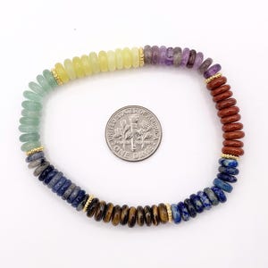 Peut inclure: Un bracelet de perles color&eacute;es avec des pierres pr&eacute;cieuses aux couleurs de l'arc-en-ciel, dont le vert, le jaune, le violet et le marron. Des entretoises dor&eacute;es ornent le bracelet. Une pi&egrave;ce de monnaie est incluse pour l'&eacute;chelle.