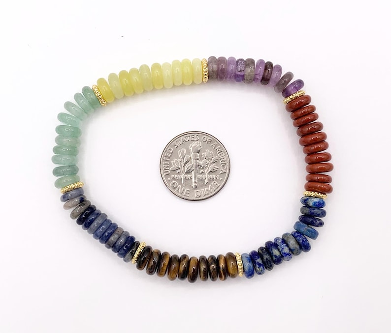 Peut inclure: Un bracelet de perles color&eacute;es avec des pierres pr&eacute;cieuses aux couleurs de l'arc-en-ciel, dont le vert, le jaune, le violet et le marron. Des entretoises dor&eacute;es ornent le bracelet. Une pi&egrave;ce de monnaie est incluse pour l'&eacute;chelle.