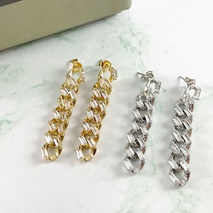 May include: Two pairs of long, dangling earrings. One pair is gold with clear cubic zirconia stones, and the other pair is silver with clear cubic zirconia stones.