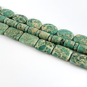 May include: A strand of green and brown jasper beads. The beads are oval and rectangular in shape.