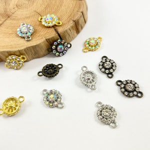 May include: Assortment of 10 silver, gold, and bronze metal connector charms with clear and iridescent rhinestones. Each charm features a flower design with two loops for attaching to jewelry.