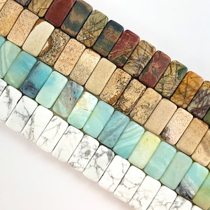 May include: Close-up of rectangular gemstone beads in various colors. The beads include white with gray veining, turquoise, light green, tan, and reddish-brown. The beads are arranged in rows, showcasing their natural patterns and textures.