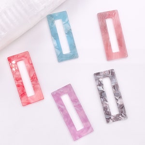 May include: Five rectangular plastic hair clips in various colors and patterns. The clips are light blue, pink, red, purple, and gray.