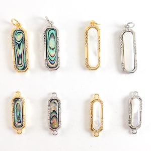 May include: Eight gold and silver pendant charms with a rectangular shape. The charms feature a white or iridescent abalone shell inlay and are accented with clear rhinestones around the edges.