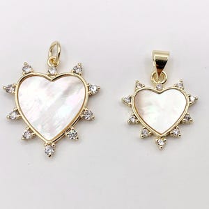 May include: Two gold heart-shaped pendants with white mother-of-pearl inlays and clear crystal accents.