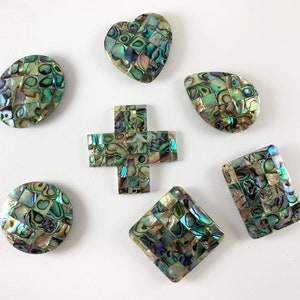 May include: Seven iridescent green, blue, and gold abalone shell mosaic tiles in various shapes, including a heart, oval, teardrop, cross, square, and rectangle.