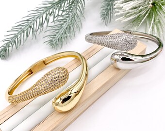 May include: Two gold and silver bangle bracelets with a teardrop design. The bracelets are adorned with clear cubic zirconia stones.