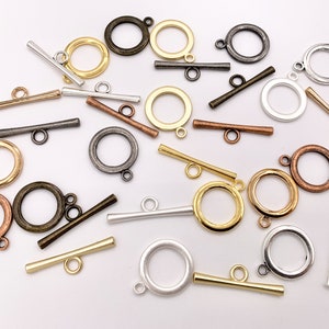 May include: Assortment of metal toggle clasps in various finishes, including silver, gold, and bronze. The clasps are in different sizes and shapes, with some featuring a round design and others with a more rectangular shape.