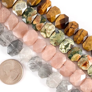 May include: A close-up of four strands of gemstone beads. The top strand is brown tiger's eye, the next is green and white ocean jasper, the third is pink rose quartz, and the bottom is clear and gray smoky quartz. The beads are faceted and have a hexagonal shape.