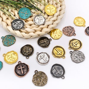 May include: A collection of 16 metal charms featuring a cross design. The charms are in various colors, including gold, silver, bronze, and turquoise. Each charm has a different texture and finish.