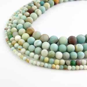 May include: A strand of various shades of green, blue, and brown round beads. The beads are made of natural stone and have a smooth, polished finish.