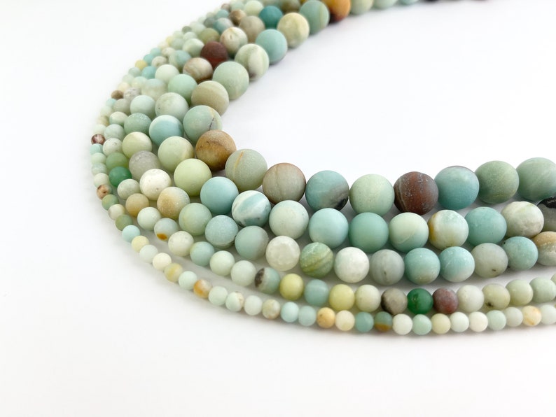 May include: A strand of various shades of green, blue, and brown round beads. The beads are made of natural stone and have a smooth, polished finish.