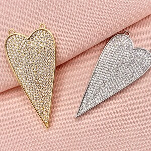 May include: Two heart-shaped pendants with a pointed bottom. Both pendants are covered in small, clear rhinestones. One pendant is gold and the other is silver.