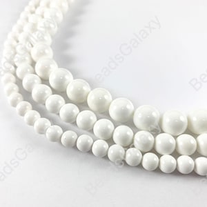 May include: A strand of white round beads, made of polished white stone. The beads are smooth and glossy, and they are strung on a clear thread.