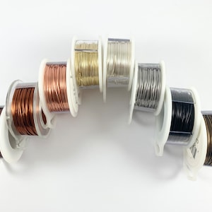 May include: Eight spools of wire in different colors, including copper, gold, silver, and black. The spools are arranged in a semi-circle on a white background.