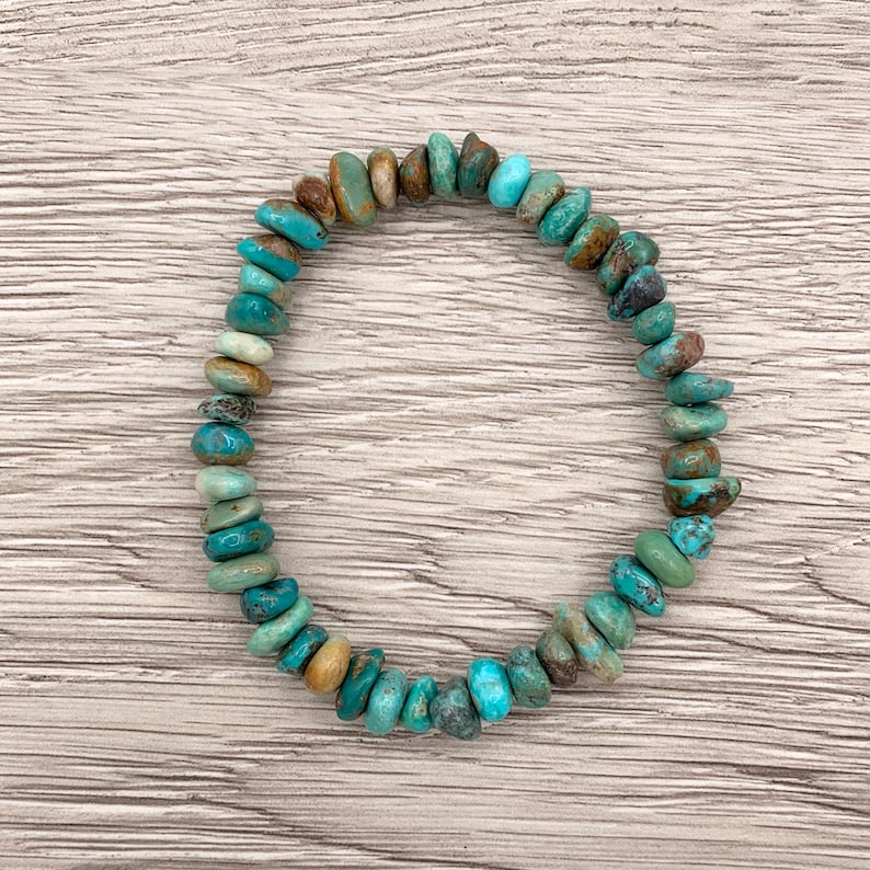 Pu&ograve; includere: Un braccialetto di perline di turchese. Il braccialetto presenta una variet&agrave; di perline di turchese nelle tonalit&agrave; del blu, del verde e del marrone. Le perline sono infilate insieme per formare una forma circolare. Il braccialetto &egrave; esposto su una superficie di legno chiaro.