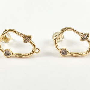 May include: A pair of gold-tone earrings with a unique, organic shape and clear crystal accents.