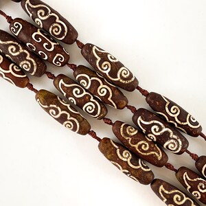 May include: A strand of brown agate beads with white cloud designs. The beads are strung on a brown cord.