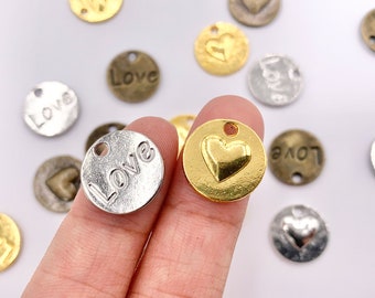 May include: Assortment of silver and gold metal charms with the word "Love" engraved on them. Some charms feature a heart design.