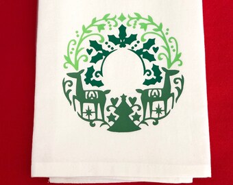 May include: White kitchen towel with a green Christmas wreath design featuring two deer, a Christmas tree, and holly leaves.