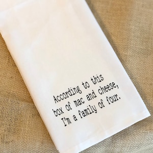 May include: White kitchen towel with black text that reads "According to this box of mac and cheese, I'm a family of four."