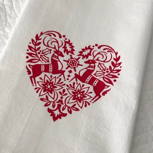 May include: White kitchen towel with a red heart-shaped design featuring two stylized reindeer with antlers and floral accents.