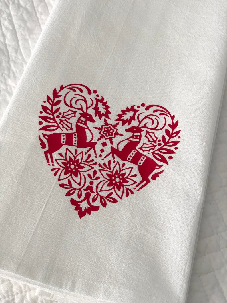 May include: White kitchen towel with a red heart-shaped design featuring two stylized reindeer with antlers and floral accents.