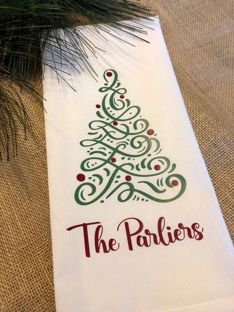 K&ouml;nnte beinhalten: Ein wei&szlig;es K&uuml;chentuch mit einem gr&uuml;nen und roten Weihnachtsbaumdesign und dem Text "The Parliers" in Rot.